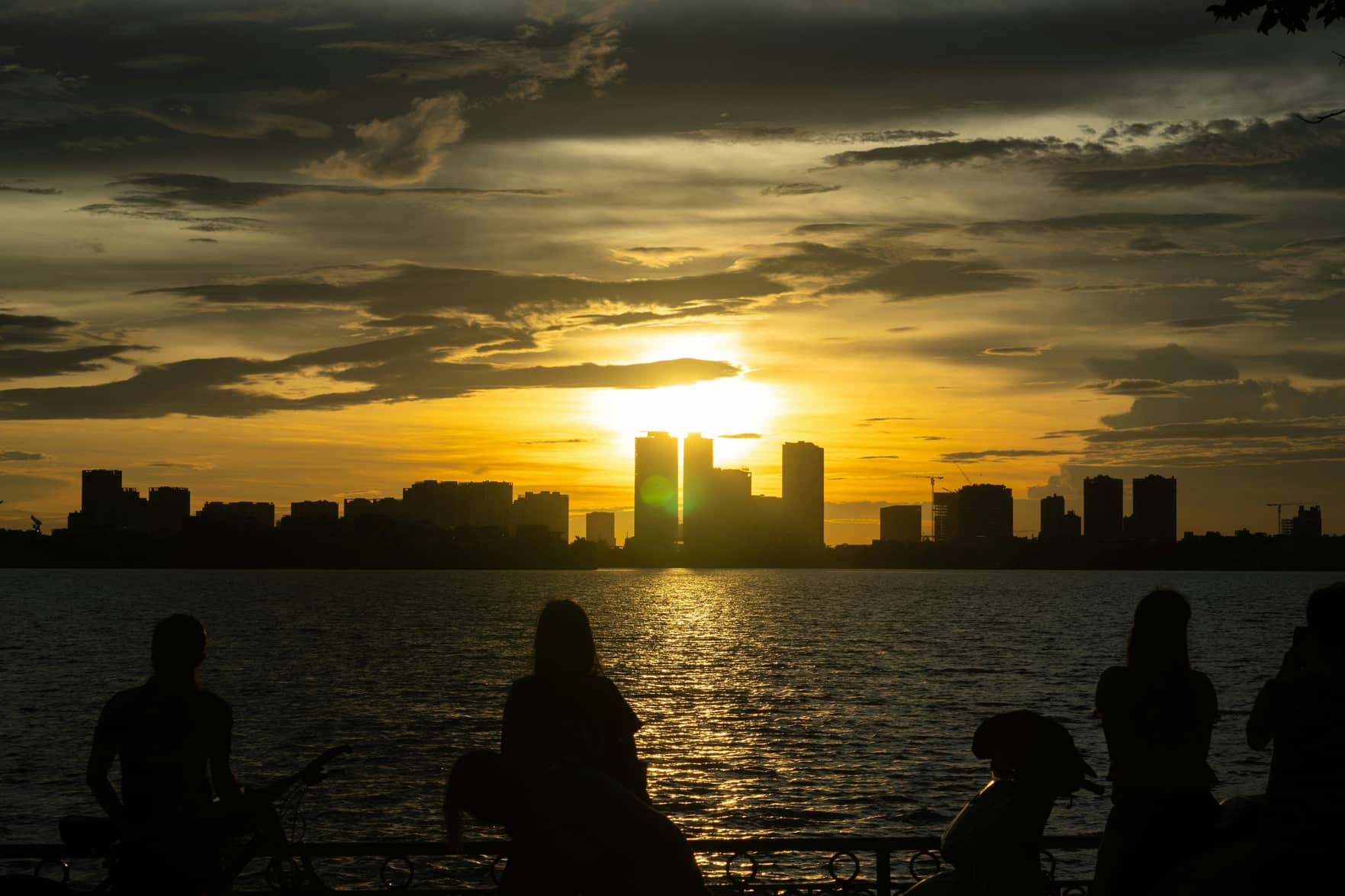 Silhouettes de promeneurs face à un coucher de soleil sur une baie et une ligne de gratte-ciel, illustration de l'horizon long terme d'un PER responsable