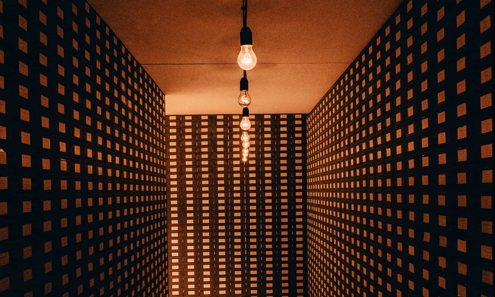 Ampoules suspendues dans un couloir géométrique, symbole de la clarté apportée par le calcul du plafond d'épargne retraite